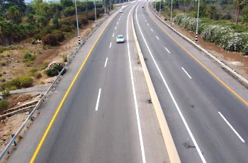צילום מלמעלה של דרך מחולקת: שני כבישים, בכל אחד שני נתיבים עם קו מרוסק, וביניהם רצועת הפרדה מוגבהת. קו צהוב רצוף בשוליים החיצוניים, מעקות בטיחות בשני הצדדים, ורכבים אחדים בכביש השמאלי.