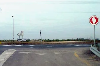 צילום של כביש פתוח וריק עם אופק רחב. בצד ימין ניצב תמרור מתומן אדום ובו ציור כף יד לבנה, ומשמאל שלטי כיוון עם סימני חץ.