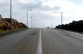 צילום של דרך בין-עירונית פנויה בין גבעות סלעיות, עם קו לבן מרוסק במרכז ועמודי תאורה בצדדים.